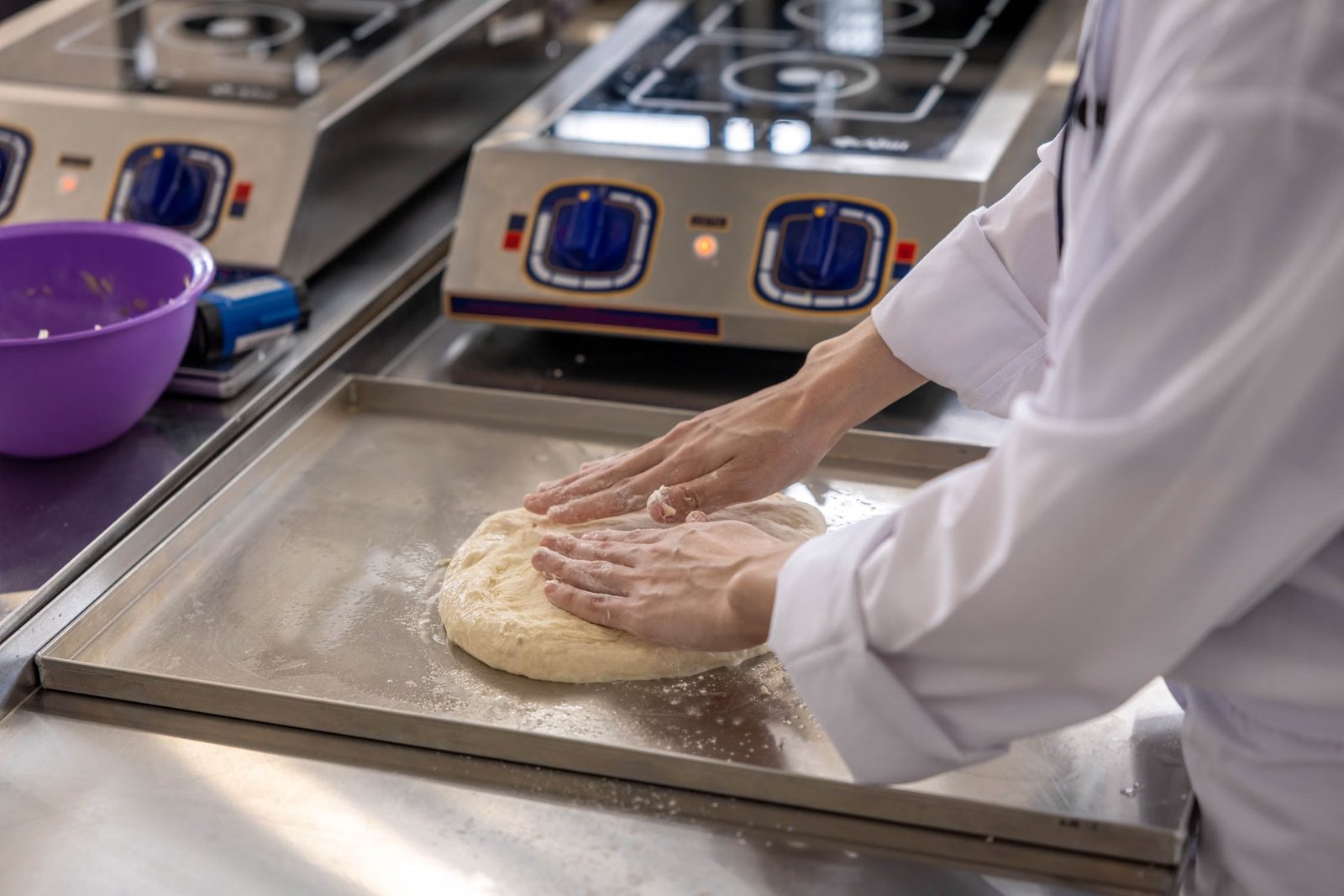 A chef preparing dough on a stainless steel work surface